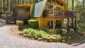 A two-story log cabin with a green roof, a wooden deck, and a stone foundation. - Cabin in the mountains with hot tub! (Ellijay)