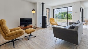A modern living room with a TV, sofa, and chairs, a fireplace, and a large sliding glass door to the outdoors.