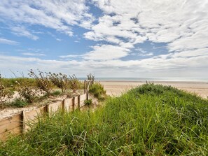 Una playa con una valla de madera y dunas cubiertas de hierba.