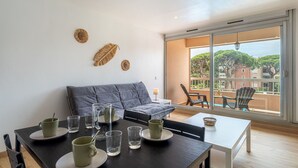 Un salon moderne avec un canapé gris, une table à manger avec de l’assiette et des verres, et une vue sur un balcon aménagé avec du mobilier d’extérieur.