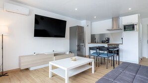 Un salon moderne doté d’un téléviseur à écran plat, d’un coin repas avec des chaises, d’une cuisine équipée d’un four à micro-ondes et d’un canapé.
