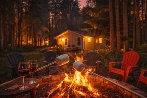 A cozy outdoor seating area with a fire pit, two glasses of red wine, and two marshmallows roasting over the flames.