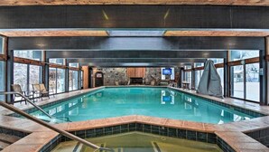 An indoor swimming pool with clear glass walls, a stone wall, and a wooden ceiling. - Four-Season Retreat at Shanty Creek Resort (Bellaire)