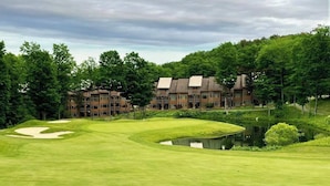 A golf course with bunkers, a pond, and a building with multiple floors in the background. - Four-Season Retreat at Shanty Creek Resort (Bellaire)