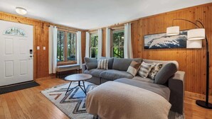 A cozy room with a wooden interior, a sofa, a coffee table, and a large window with curtains. - Four-Season Retreat at Shanty Creek Resort (Bellaire)