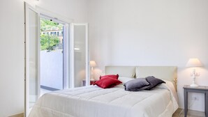 A bedroom with a bed, two bedside lamps, a nightstand, and a sliding glass door leading to an outdoor area.