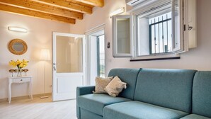 A modern living room with a teal sofa, a small white side table with a lamp, and a door leading to another room.