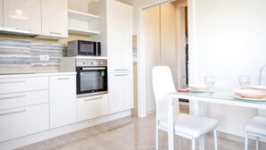 A modern kitchen with white cabinetry, a built-in microwave, oven, and a glass dining table with white chairs.