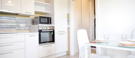 A modern kitchen with white cabinetry, a built-in microwave, oven, and a glass dining table with white chairs.