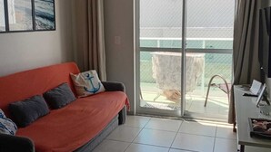 Un salon comprenant un canapé, une table, une fenêtre et une porte donnant sur un balcon.