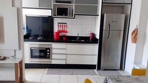 Une cuisine moderne avec des meubles blancs, un four à micro-ondes, une cuisinière et un réfrigérateur. On y trouve également un coin repas avec une chaise jaune et une table recouverte d’une nappe à motifs.