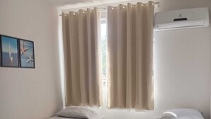 Une chambre avec deux lits, une chaise, une fenêtre avec des rideaux et un appareil de climatisation.