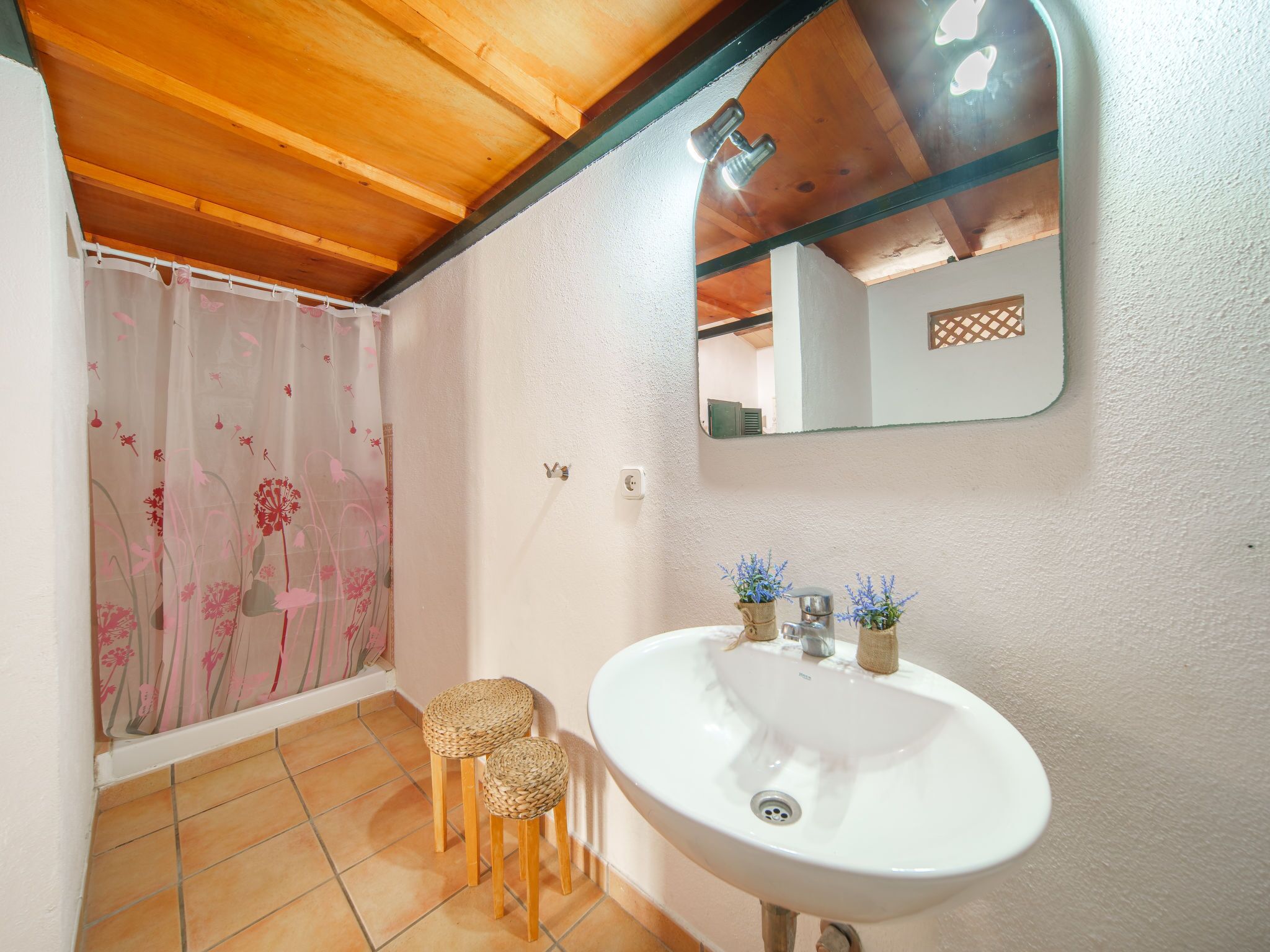 Ein Badezimmer mit einem weißen Waschbecken, zwei Korbstühlen, einem Duschvorhang mit Blumenmuster und einem Spiegel über dem Waschbecken.