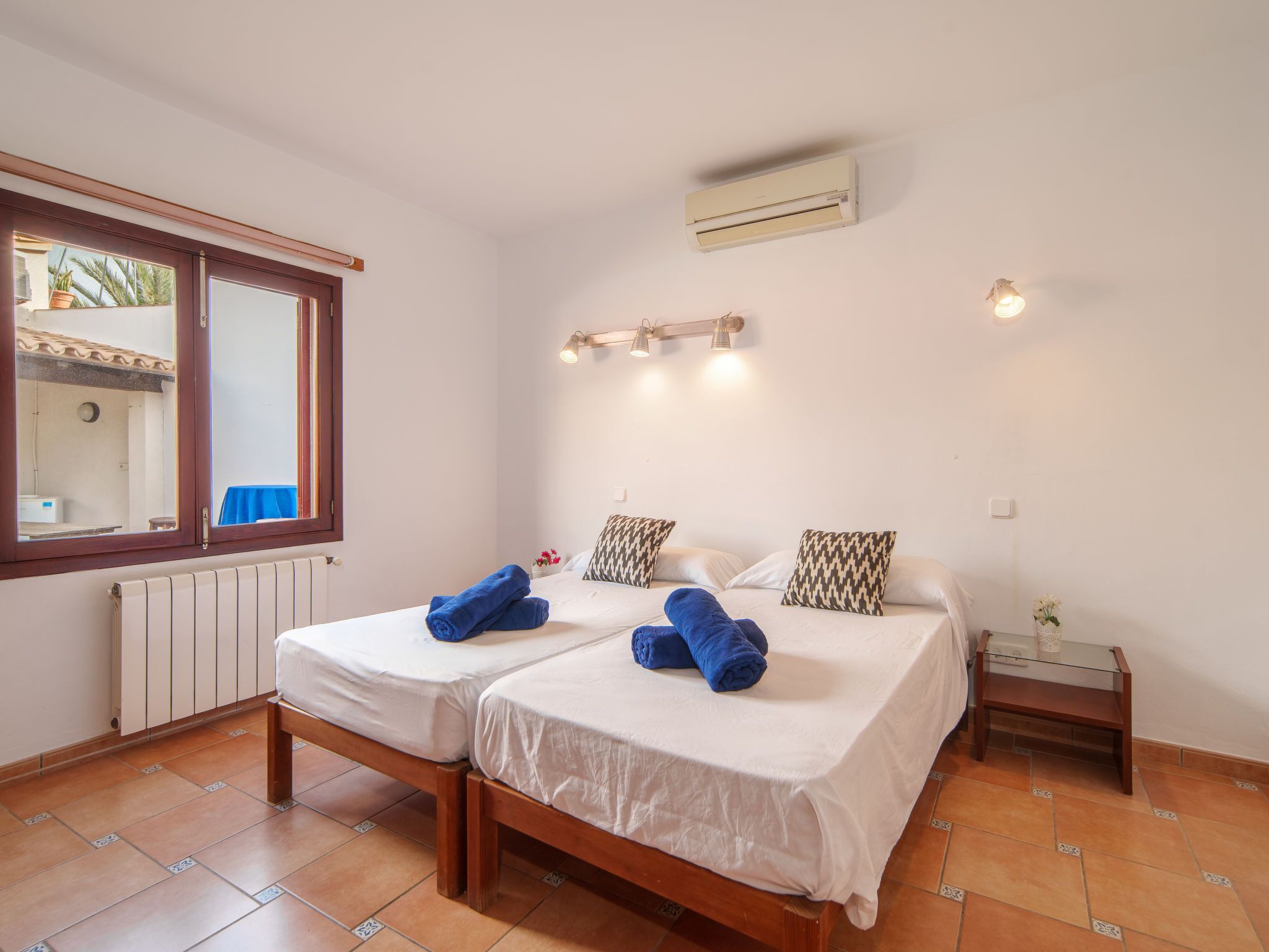 Een kamer met twee bedden, een raam, een airconditioner en een klein nachtkastje.