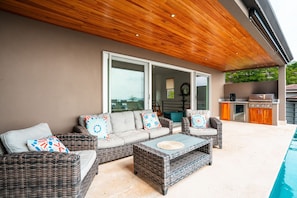An outdoor patio with wicker furniture, a pool, and a barbecue area.
