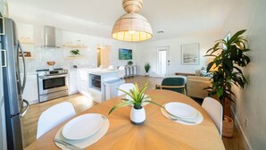 A modern kitchen with white cabinets, a central island, and a dining area with a wooden table and chairs. - The Coconut Palm | 5 Minutes to Bonita Beach (Bonita Springs)
