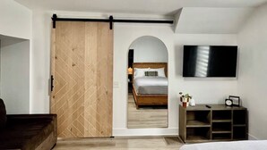 Une chambre moderne avec un plancher en bois, un lit, une télévision et une porte coulissante donnant sur une autre pièce.
