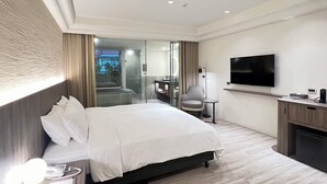A modern hotel room with a large bed, a TV, a desk, and a glass shower area. - Crownshine Resort (Jiaoxi)