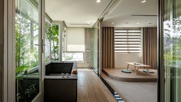 A modern interior with a long hallway, a seating area with a table, and a large window with plants. - Crownshine Resort (Jiaoxi)