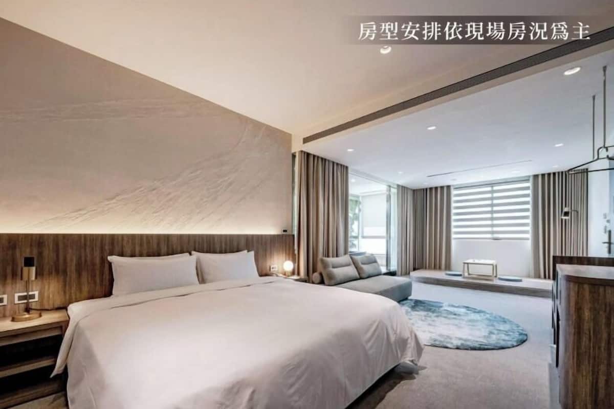 A modern hotel room with a large bed, a seating area, and a view of the outdoors.