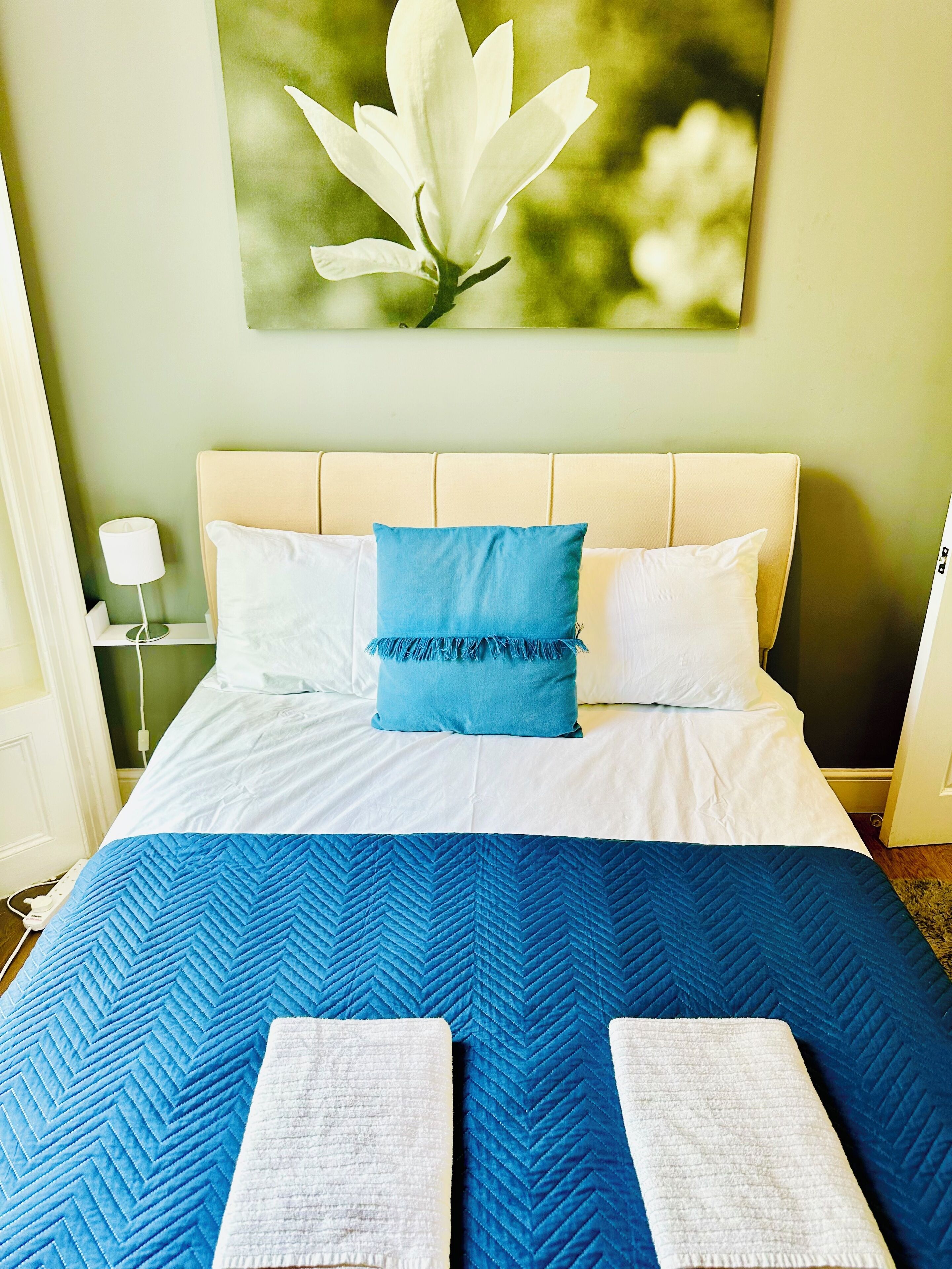 Una cama bien hecha con colcha azul, almohadas blancas y un cojín decorativo azul.