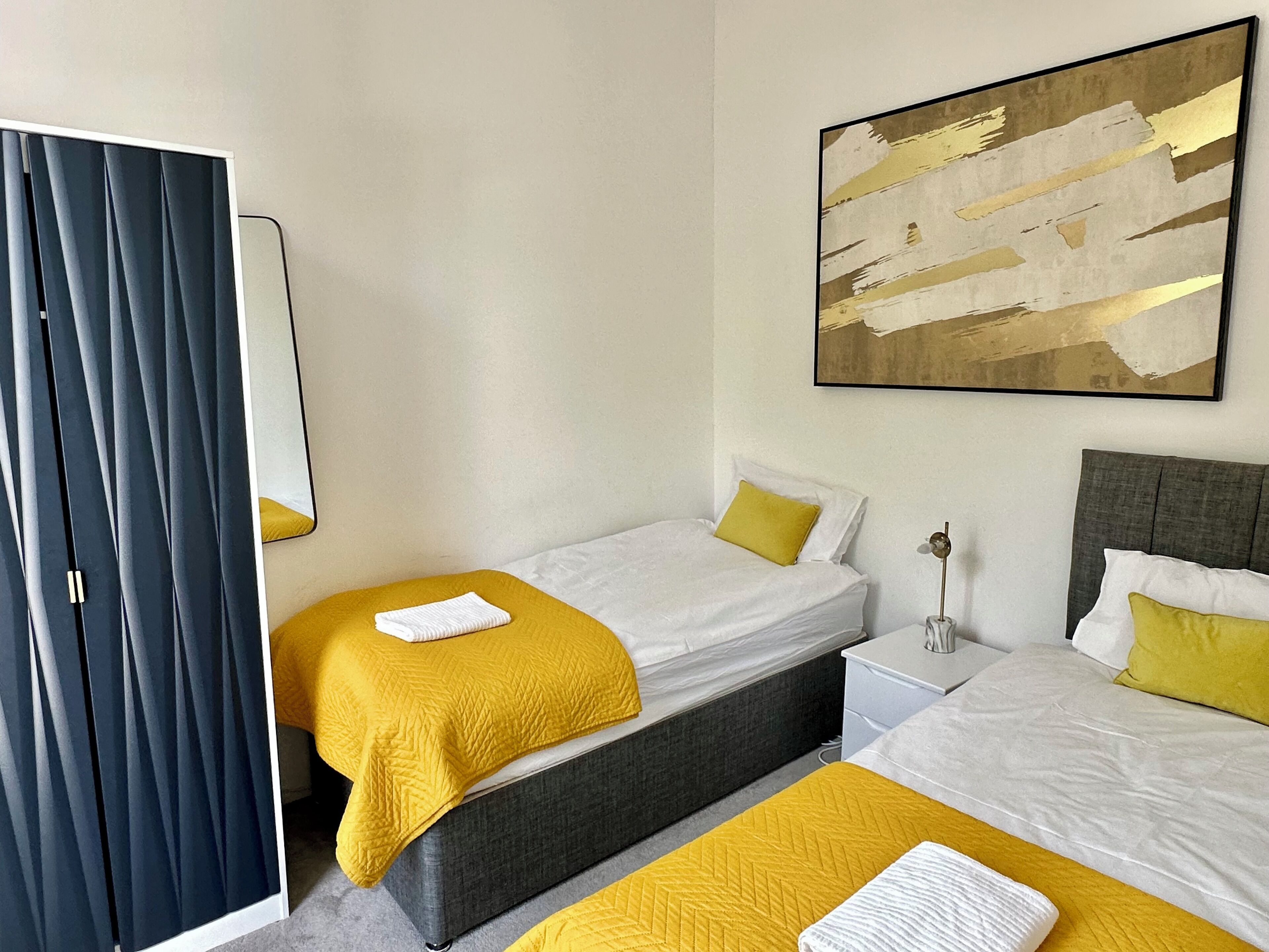 A hotel room with two beds, a large abstract painting, a mirror, and a window with curtains.