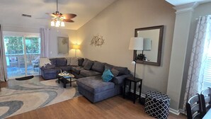 Una sala de estar con un sofá modular, una mesa de centro, un televisor y un ventilador de techo.
