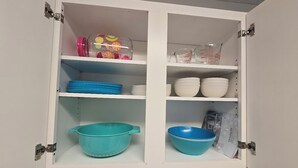 Un armario de cocina con estantes que contiene utensilios de cocina, incluyendo cuencos, platos y un colador.