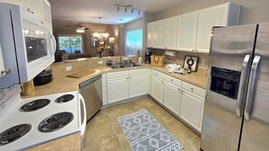 Una cocina moderna con armarios blancos, un refrigerador de acero inoxidable, horno empotrado y microondas.