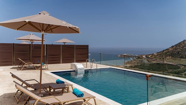 Zona de piscina con sillas de descanso y sombrillas, una piscina pequeña y vistas a la costa.