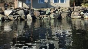 A two-story house with a balcony, a stone foundation, and a body of water in front. - Oceanfront🔹Abundant Wildlife Viewing Opportunities🔹Local Native Owners (Ketchikan)
