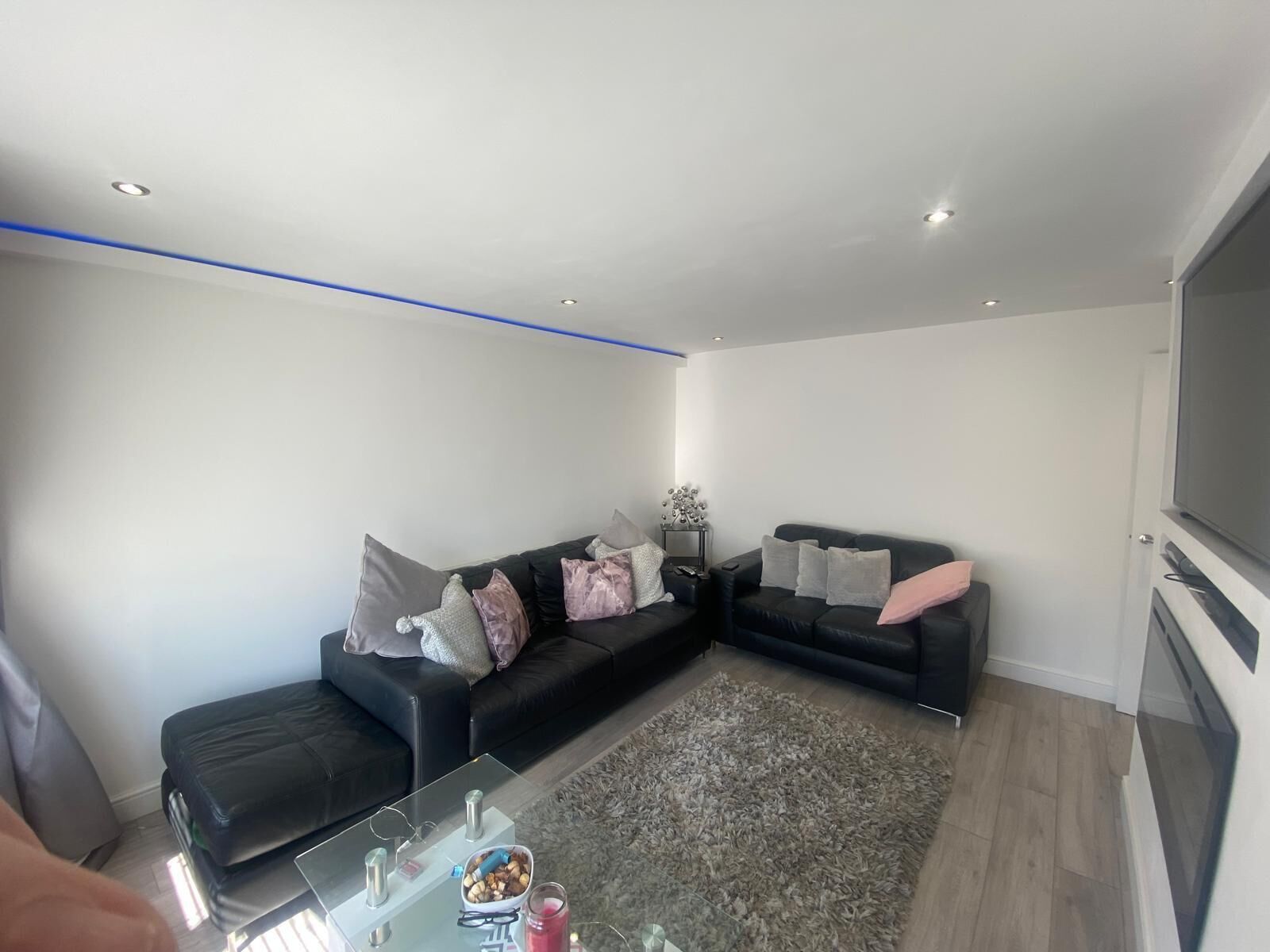 A modern living room with a sectional sofa, a glass coffee table, and a flat-screen TV.
