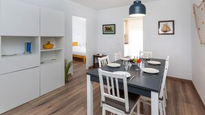 Une cuisine moderne avec des meubles blancs, une table à manger pour quatre personnes et un luminaire suspendu.