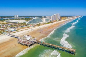 A coastal cityscape with a beach, a pier, and high-rise buildings.