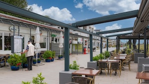 Ein Café mit Sitzgelegenheiten im Freien, ein überdachter Gang und ein Restaurant im Hintergrund.