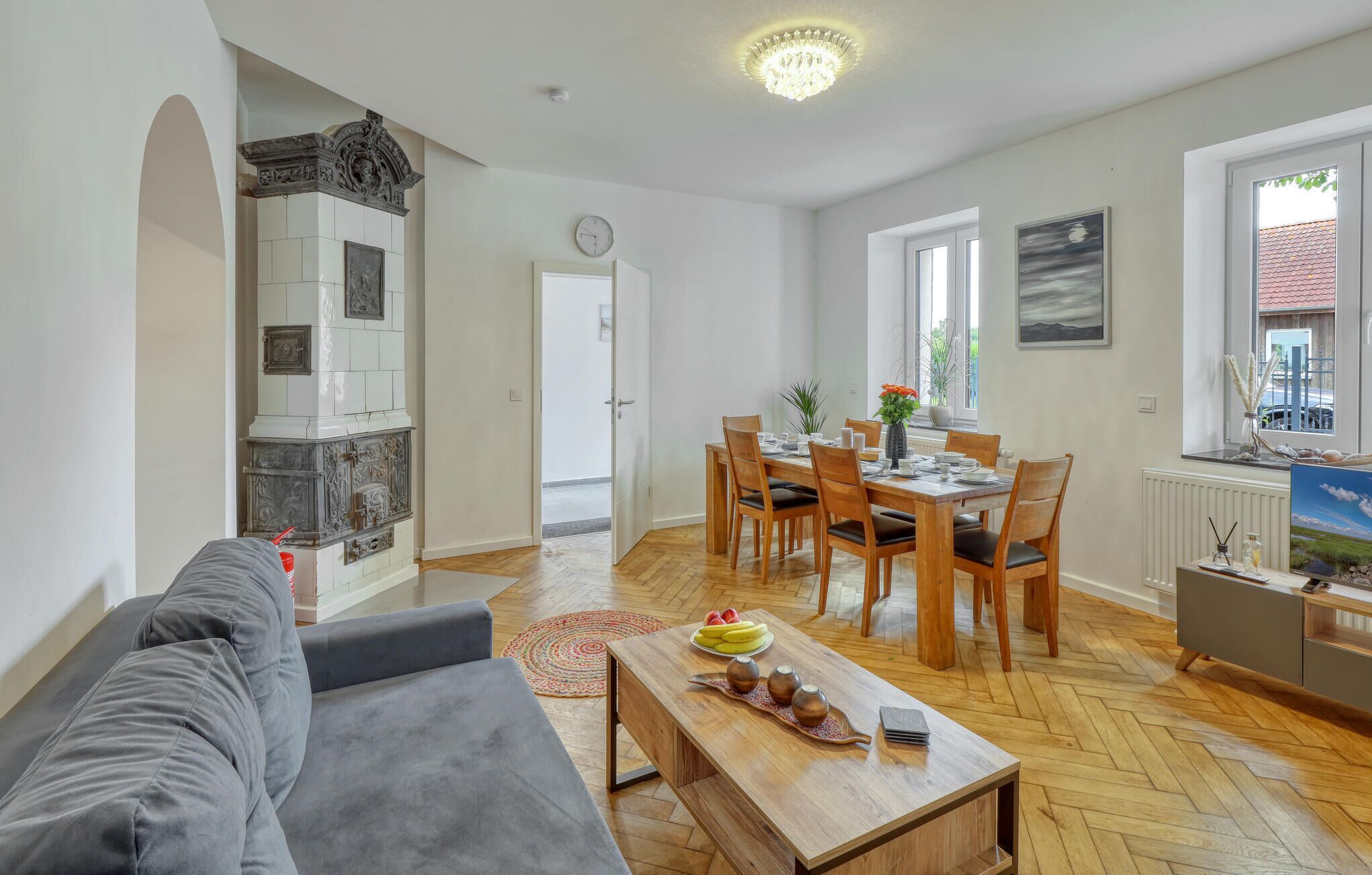 A spacious living area with a sofa, a wooden dining table set for four, and a kitchen with a decorative stove.