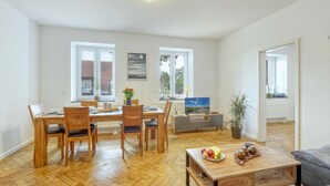 A spacious living room with a dining area, large windows, and a view of the outside. - 3 bedroom cozy apartment in Großenbrode (Großenbrode)