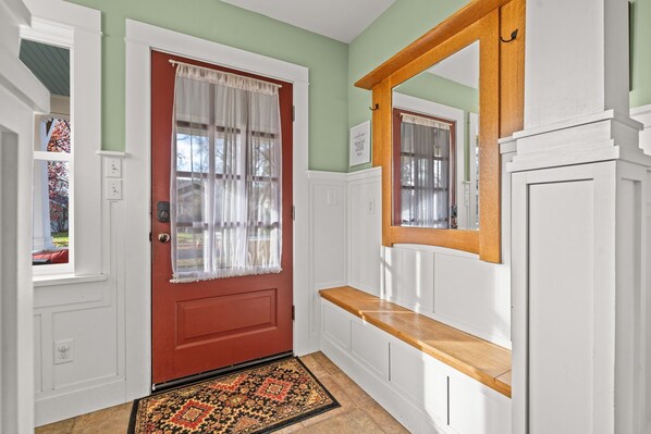 Un couloir avec une porte rouge, des moulures blanches, un banc en bois et un tapis à motifs.