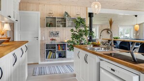 A modern kitchen with wooden cabinets, a central island with a sink, and a dining area with a black chair.