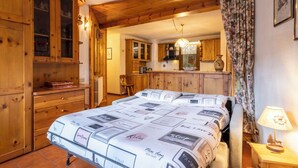 A cozy bedroom with a large bed, wooden cabinets, and a kitchen in the background. - Erica Apartment by Interhome (Bormio)