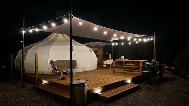 A tent with a wooden deck, string lights, and a table.
