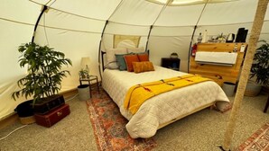 A cozy tented room with a bed, a bedside table, a lamp, a plant, and a suitcase.