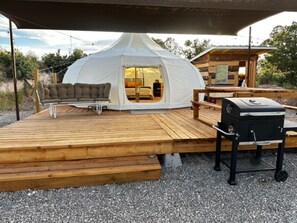 Une tente blanche avec un canapé et un barbecue sur une terrasse en bois.