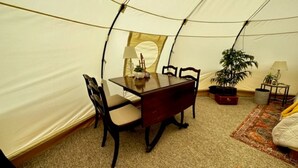 A tent with a dining table and chairs, a lamp, and a potted plant.