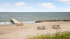 Una spiaggia sabbiosa con un molo di legno che si protende nell'acqua, con tre tavoli da picnic.