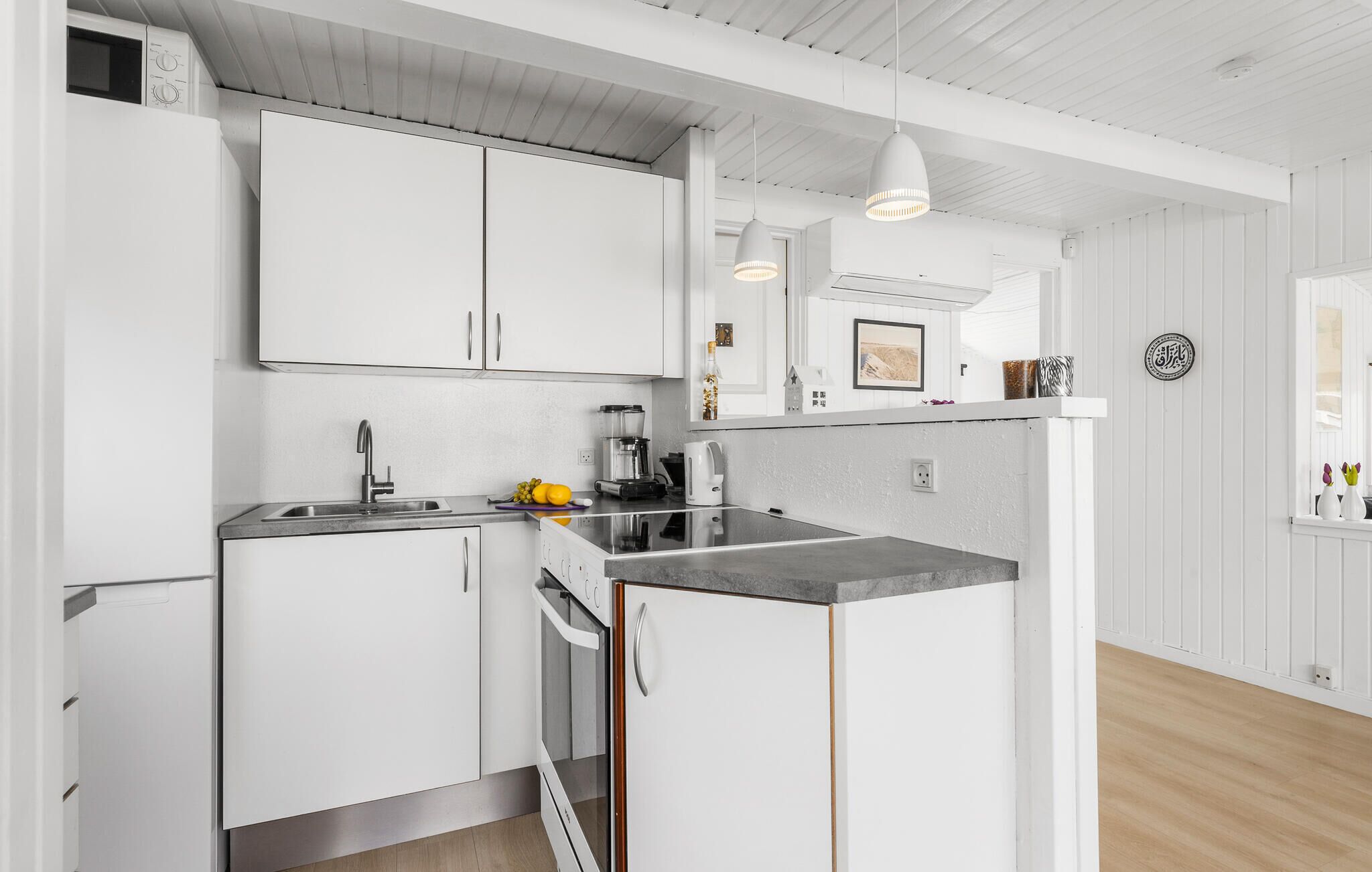 A modern kitchen with white cabinetry, a built-in oven, a sink, and a countertop with a coffee maker and fruit.