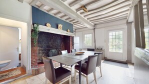 A dining area with a brick fireplace, white ceiling beams, and a large window. - 3 bedroom nice home in Vittefleur (Vittefleur)