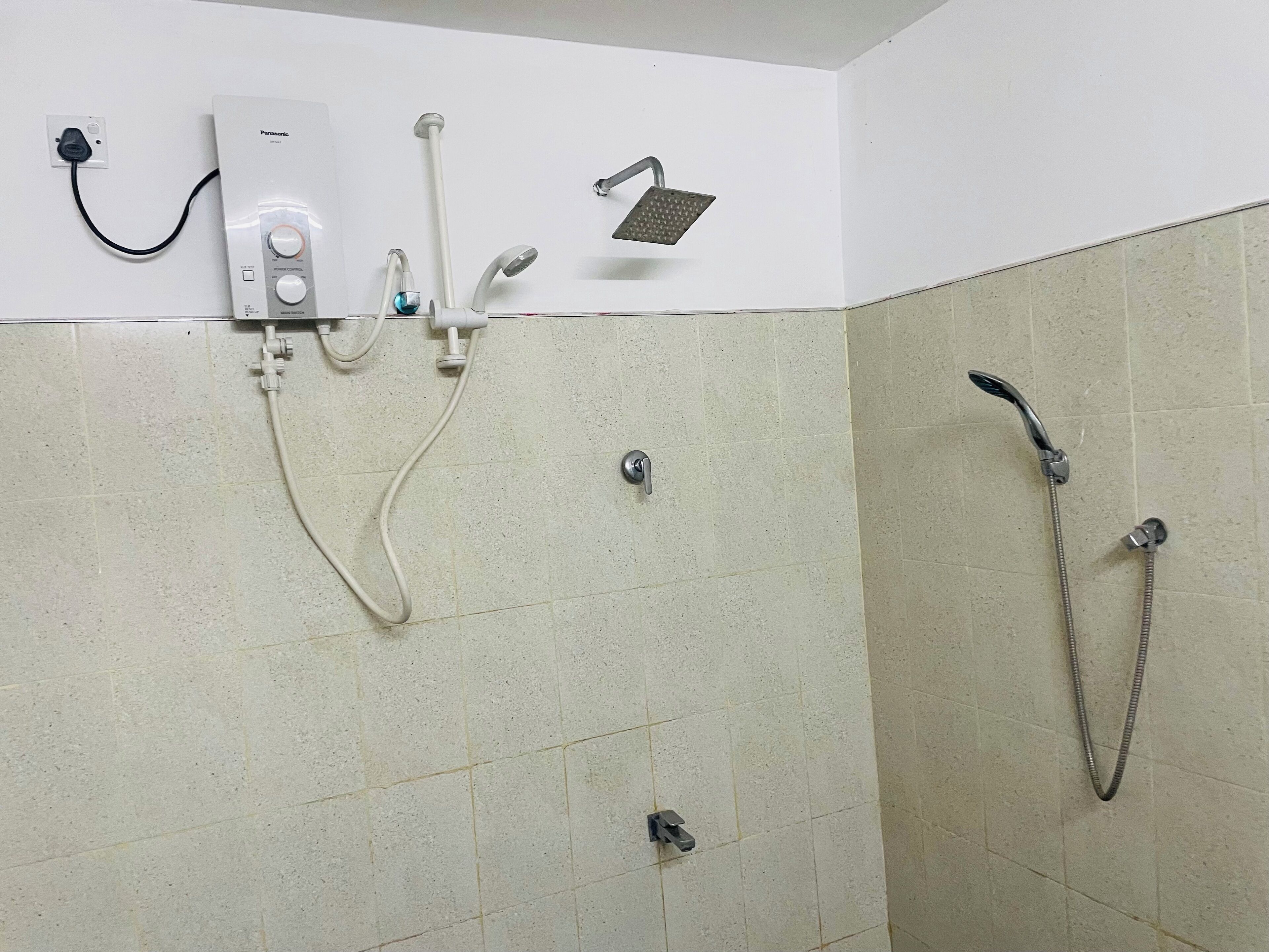 A bathroom with a shower, a handheld showerhead, a wall-mounted faucet, and a control panel.