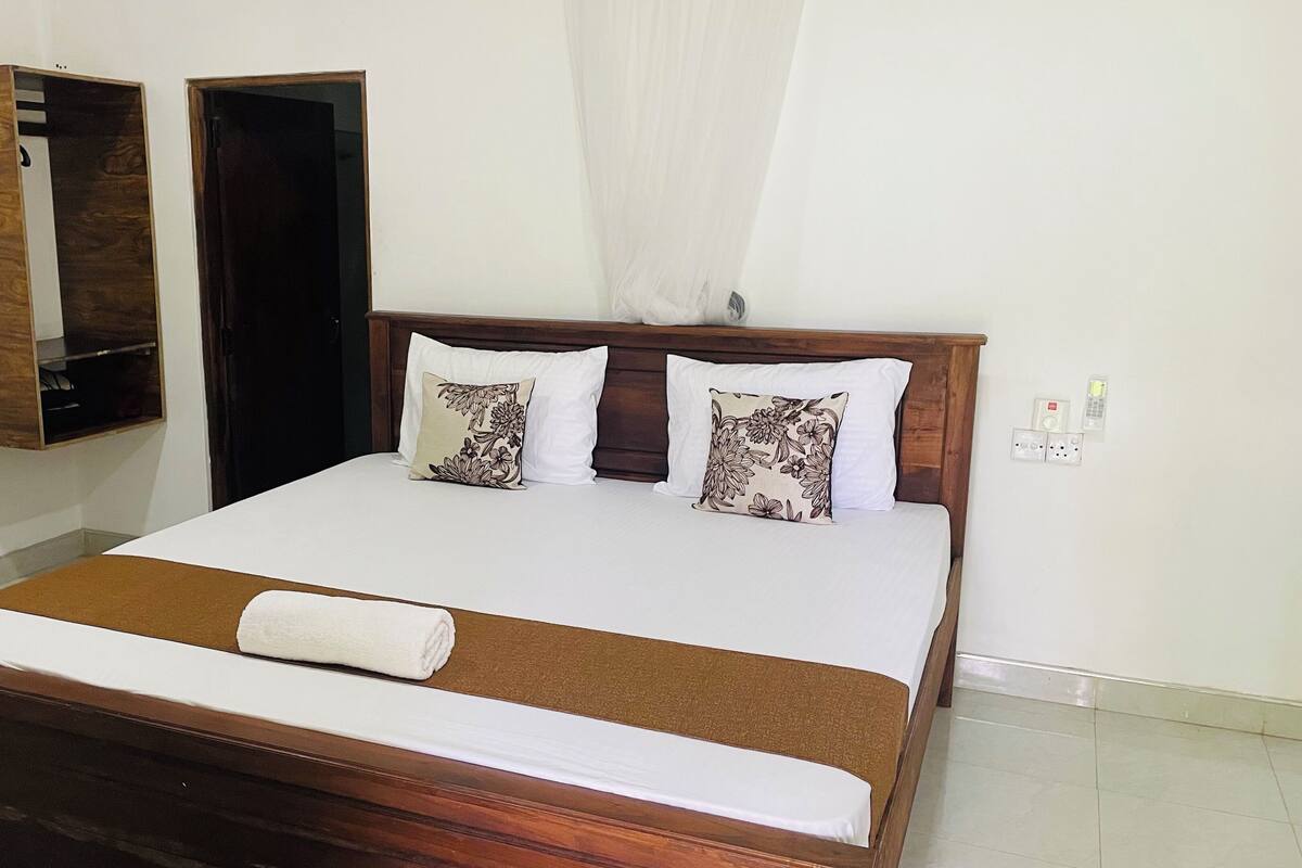 A neatly made bed with a brown headboard, two decorative pillows, and a white towel.