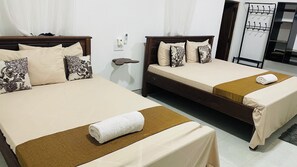 A hotel room with two beds, each with a brown headboard, beige bedding, and floral-patterned pillows. A white towel is placed on the bed in the foreground. - Sigiri Suncap Cottage (Diganpathaha)